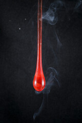 Gota de vidro vermelho semi transparente em fundo preto. Fotografia em close up de uma peça similar a um líquido de alta viscosidade pingando.