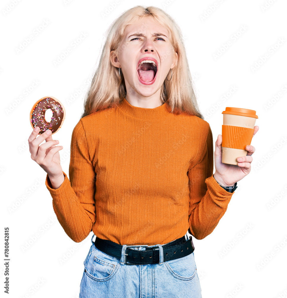 Wall mural young caucasian woman eating doughnut and drinking coffee angry and mad screaming frustrated and fur