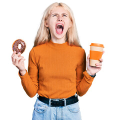 Young caucasian woman eating doughnut and drinking coffee angry and mad screaming frustrated and furious, shouting with anger looking up.