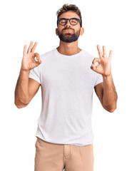 Fototapeta premium Young hispanic man wearing casual clothes and glasses relaxed and smiling with eyes closed doing meditation gesture with fingers. yoga concept.