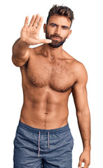 Young hispanic man wearing swimwear shirtless doing stop sing with palm of the hand. warning...
