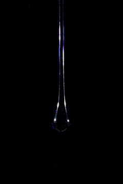 Gota de vidro azul semi transparente em fundo preto. Fotografia em close up de uma peça similar a um líquido de alta viscosidade pingando.