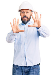 Young handsome man wearing architect hardhat afraid and terrified with fear expression stop gesture with hands, shouting in shock. panic concept.