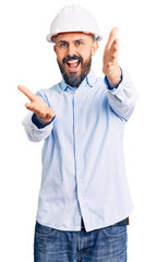 Young handsome man wearing architect hardhat looking at the camera smiling with open arms for hug. cheerful expression embracing happiness.