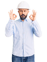 Young handsome man wearing architect hardhat relax and smiling with eyes closed doing meditation gesture with fingers. yoga concept.