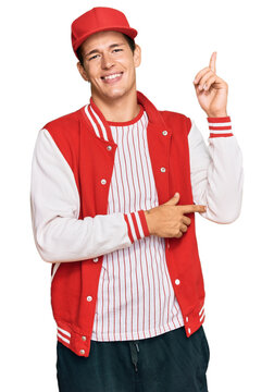 Handsome caucasian man wearing baseball uniform with a big smile on face, pointing with hand and finger to the side looking at the camera.