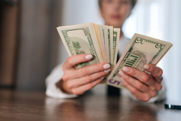 Selective focus of female counting money cash dollars bills one, five, ten, twenty and one hundred dollar banknote sitting at table. Concept of financial accounting budget planning, revenue, wealth