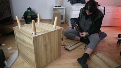 Woman Assembling Furniture in New Home, Using Drilling Machine for Nightstand Construction,...
