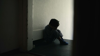 Sad and Lonely Young Child Sitting in Dark Hallway, Hiding Face in Hands, Symbolizing Emotional...