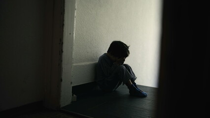Sad and Lonely Young Child Sitting in Dark Hallway, Hiding Face in Hands, Symbolizing Emotional...