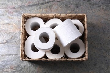 Toilet paper rolls in wicker basket on textured table, top view - obrazy, fototapety, plakaty
