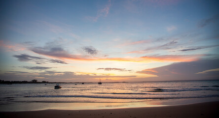 Pôr-do-sol na linha do mar, com barcos e navios no horizonte e degradê colorido de nuvens no nordeste brasileiro. Céu alaranjado e roxo. 