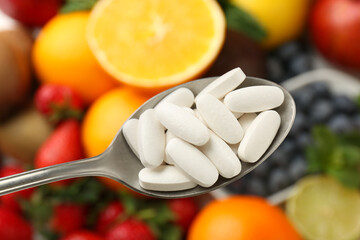 Vitamin pills in spoon over fresh fruits, closeup