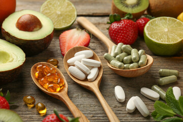 Different vitamin pills and fresh fruits on old wooden table