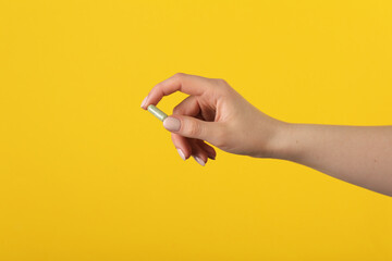 Woman holding vitamin pill on yellow background, closeup. Health supplement - obrazy, fototapety, plakaty