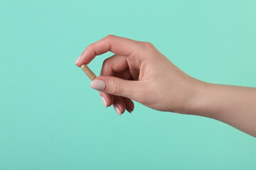 Woman holding vitamin capsule on turquoise background, closeup. Health supplement