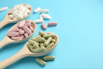 Different vitamin pills in spoons on light blue background, closeup. Space for text