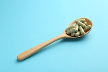 Vitamin capsules in wooden spoon on light blue background