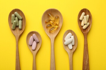 Different vitamin pills in spoons on yellow background, flat lay