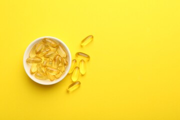 Vitamin capsules in bowl on yellow background, flat lay. Space for text