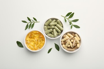 Different vitamin capsules in bowls and leaves on white background, flat lay - obrazy, fototapety, plakaty