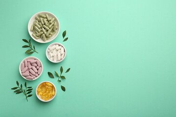 Different vitamin capsules in bowls and leaves on turquoise background, flat lay. Space for text