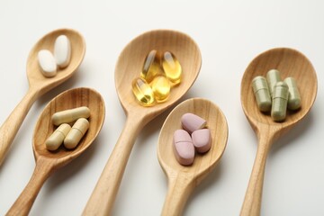 Vitamin capsules in wooden spoons on white background, closeup