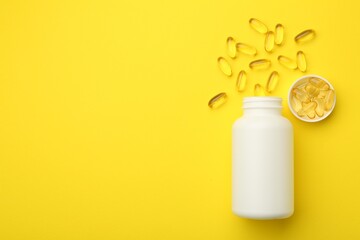 Softgel capsules, lid and bottle on yellow background, flat lay. Space for text