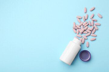 Vitamin pills, lid and bottle on light blue background, flat lay. Space for text