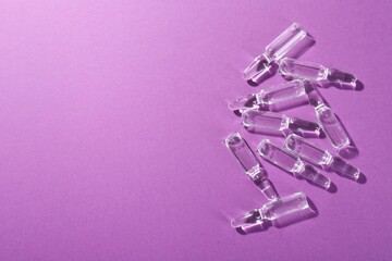 Glass ampoules with liquid on purple background, top view. Space for text