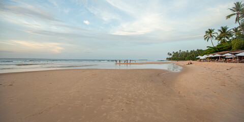 Praia do nordeste brasileiro com banhistas e luz suave de entardecer. Amigos jogando futebol na areia