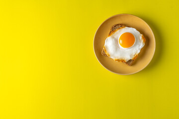 Fried egg on bread toast on a plate and on a yellow background. Top view with space for text. Flat lay.