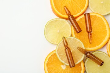 Skincare ampoules with vitamin C, lemon and orange slices on white background, flat lay. Space for...