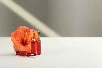 Skincare ampoules and hibiscus flower on white table. Space for text - obrazy, fototapety, plakaty