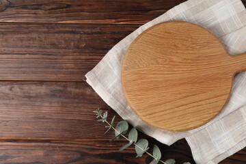 Cutting board, eucalyptus branch and napkin on wooden table, top view. Space for text
