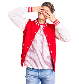 Young handsome man wearing baseball uniform covering eyes with hands smiling cheerful and funny. blind concept.