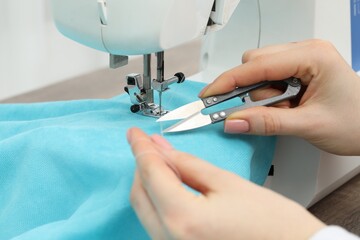 Seamstress with tailor's scissors working with sewing machine indoors, closeup