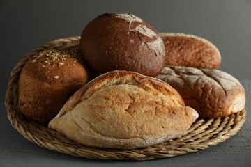 Wicker basket with different types of fresh bread on grey wooden table, closeup