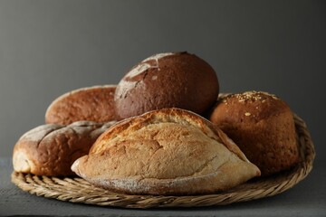 Wicker basket with different types of fresh bread on grey wooden table, closeup - obrazy, fototapety, plakaty