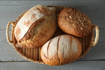 Wicker basket with different types of fresh bread on grey wooden table, top view