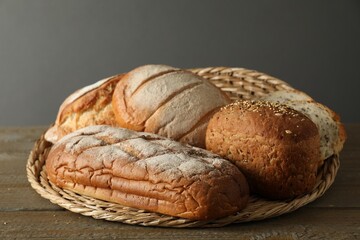 Wicker basket with different types of fresh bread on wooden table, closeup