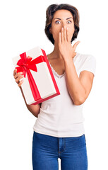 Fototapeta premium Young beautiful woman holding gift covering mouth with hand, shocked and afraid for mistake. surprised expression