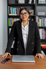 Portrait of Hispanic boss standing at her desk looking at camera smiling