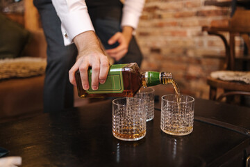 Process of man pouring whiskey in stylish glasses. Background of brick wall