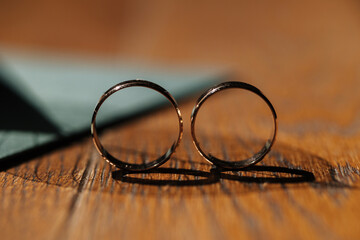 Two golden wedding rings stand together on wooden table. Sun shines on rings. Shadow from rings