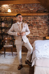Portrait of elegant groom in stylish retro hotel. Handsome man in light colour suit