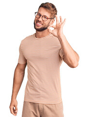 Young caucasian man wearing casual clothes and glasses smiling positive doing ok sign with hand and...