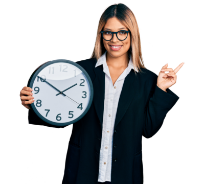 Young hispanic woman holding big clock smiling happy pointing with hand and finger to the side