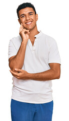 Young arab man wearing casual clothes looking confident at the camera smiling with crossed arms and hand raised on chin. thinking positive.