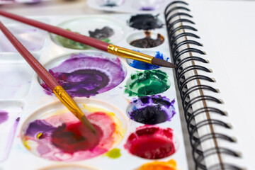 Close up view of watercolor paint with two brushes laying across the pallet.